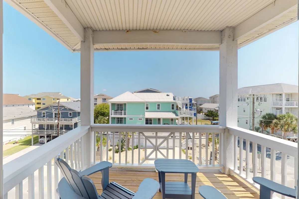 A breezy porch scene with comfortable seating and clear views of neighboring houses under a blue sky. The inviting furniture hints at leisurely mornings with coffee or evenings recapping the day's adventures, perfectly blending indoor comfort with outdoor enjoyment.