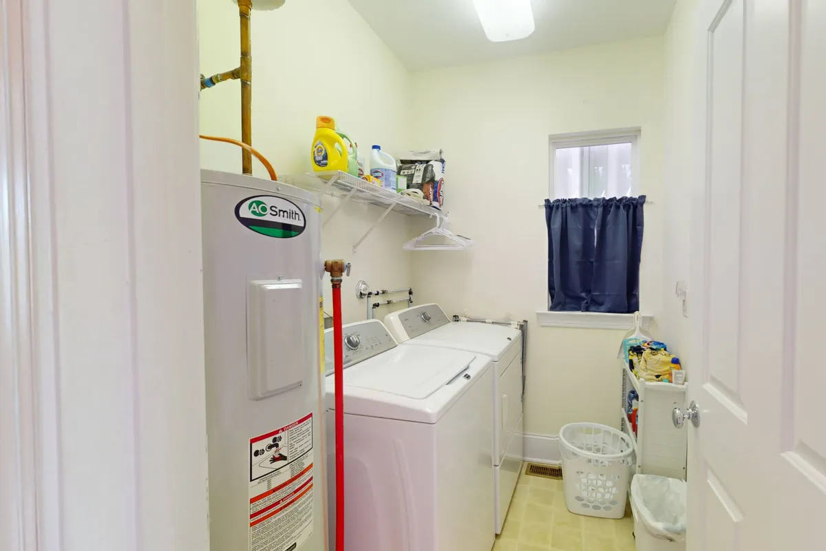 A bright and tidy laundry area featuring a washing machine and dryer, a practical storage shelf, a window providing natural light, and a laundry basket neatly tucked to the side. The clean design and organized space emphasize ease and convenience for guests managing their beachwear.