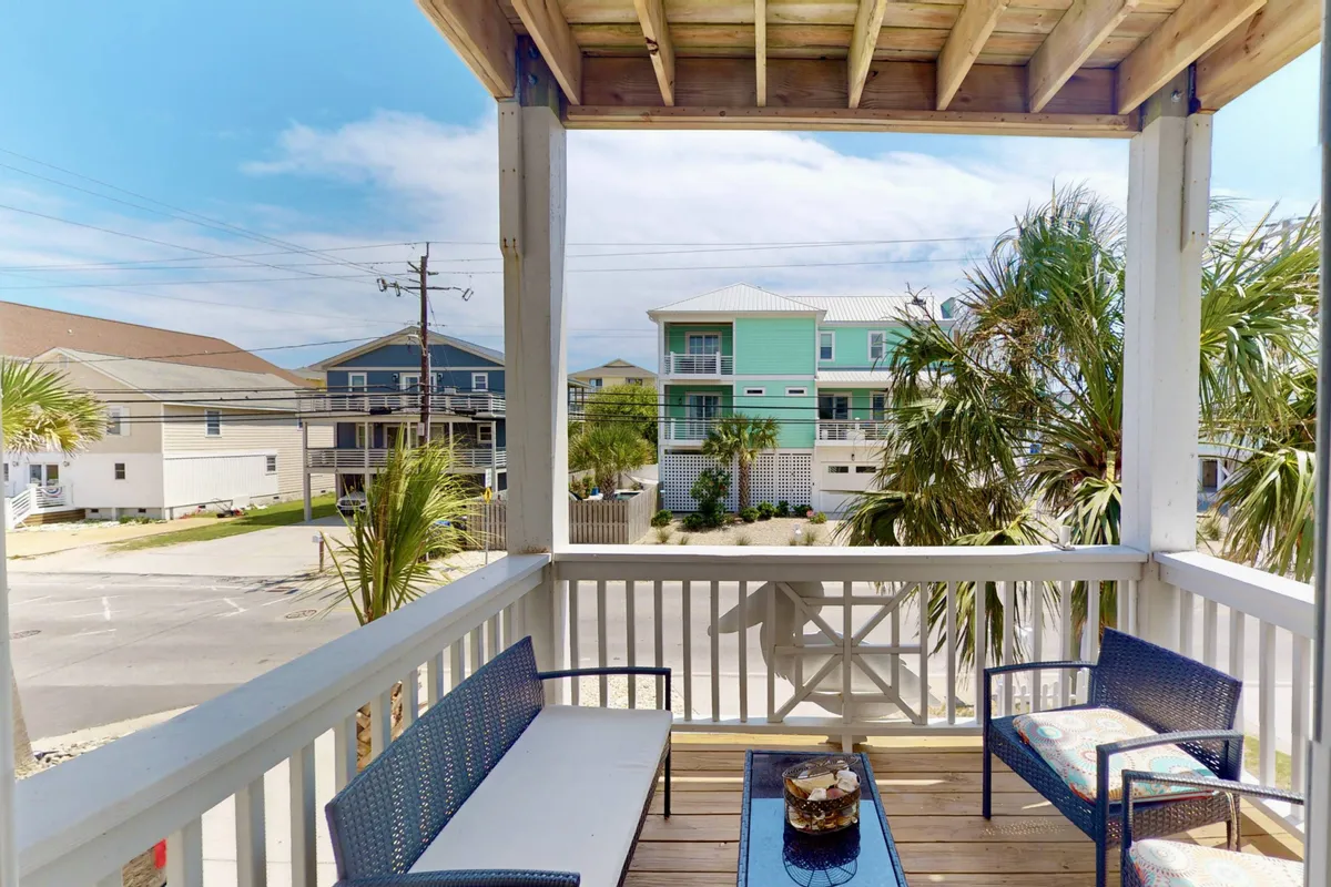 This image centers on an inviting outdoor seating area surrounded by palm trees, with neighboring houses and a blue sky in the background. It captures a casual, social atmosphere ideal for morning coffee, relaxing with a book, or enjoying meals in the open air.