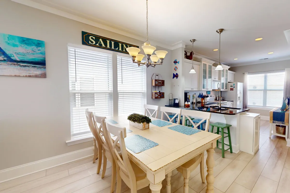 A bright dining area with a central wooden table surrounded by chairs, set adjacent to a modern kitchen. Attention-grabbing artwork and stylish light fixtures provide a cheerful, homey atmosphere—perfect for shared meals and celebrations.