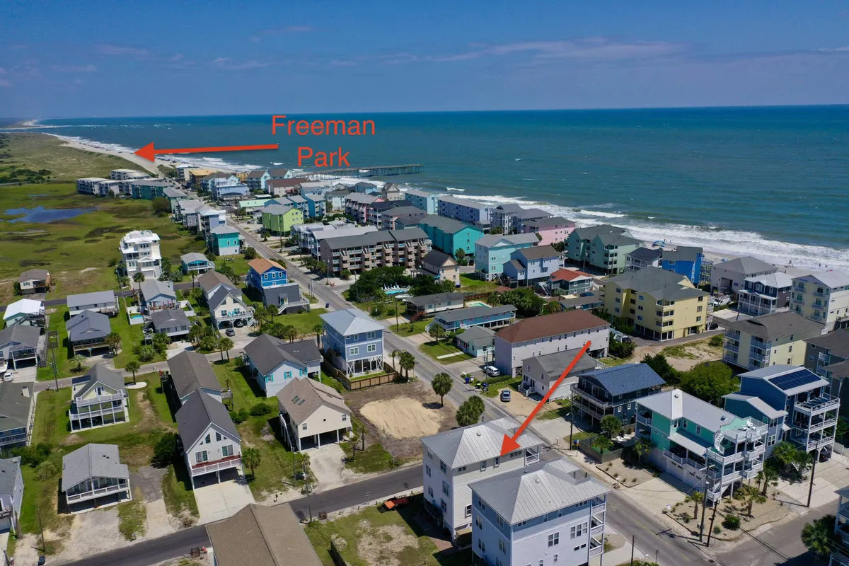 A vibrant exterior shot featuring Freeman Park, the sandy shoreline, and colorful beach houses lining the coast. People are visible enjoying the beach, emphasizing the area's relaxed, family-friendly vibe and proximity to local amenities.