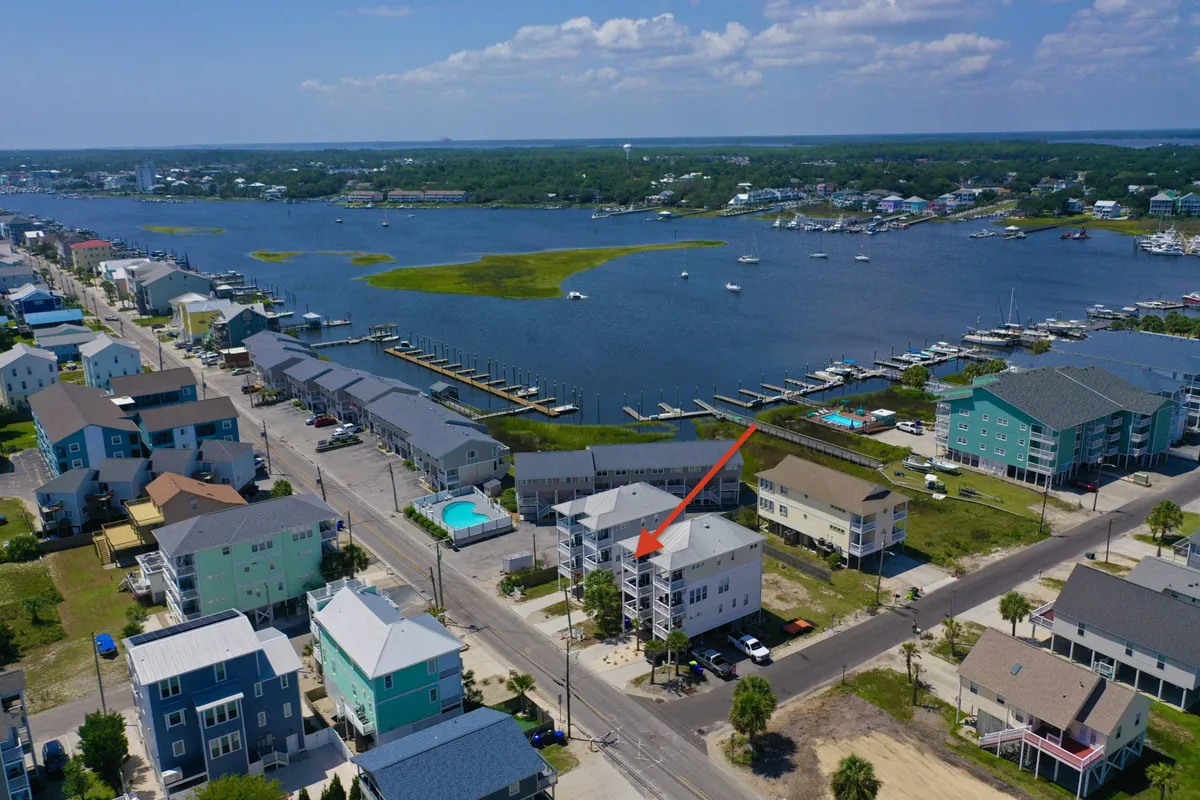 A vibrant marina lined with colorful houses, boats docked along the waterfront, a sparkling pool, and family-friendly spaces. The atmosphere is lively and relaxed, ideal for boating, fishing, swimming, and leisurely walks by the water.