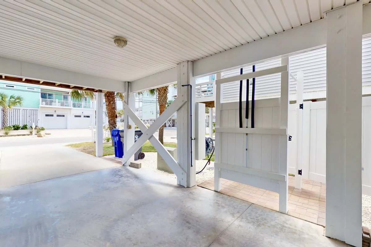 A versatile ground-level area with exposed support beams, an outdoor shower for rinsing off sand, and a handy side gate for storing beach gear. The space can also accommodate vehicle parking, visible by the open, accessible layout.