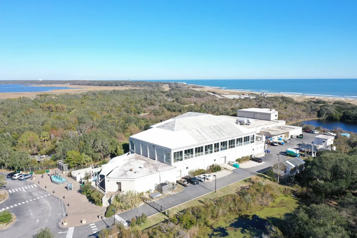 A large building set against lush greenery, with the ocean visible in the background. The area evokes a sense of history and natural beauty, suitable for exploring local landmarks, nature trails, and observing wildlife.